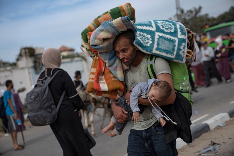 a man can be seen carrying a child with a large pack and blankets on his back