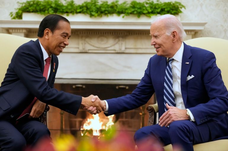 Jokowi and Biden shaking hands. There is a roaring fire in the hearth behind them. They are smiling and look relaxed.