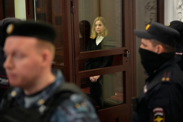 Darya Trepova standing in a glass walled dock in a military court in St Petersburg. There are soldiers keeping guard.