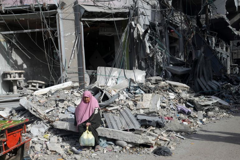 A Palestinian woman sits by buildings destroyed in the Israeli bombardment of the Gaza Strip in Nusseirat refugee camp, central Gaza Strip, Saturday, Nov. 25, 2023. on the second day of the temporary ceasefire between Hamas and Israel. (AP Photo/Adel Hana)