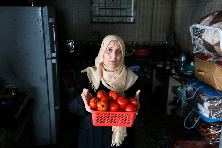 Siham Naji holds up a box of tomatoes in her kitchen that has largely remained intact