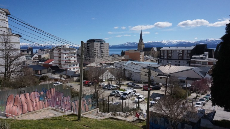 The skyline of Bariloche, Argentina, where a steeple, a lake and mountains can be seen in the distance.