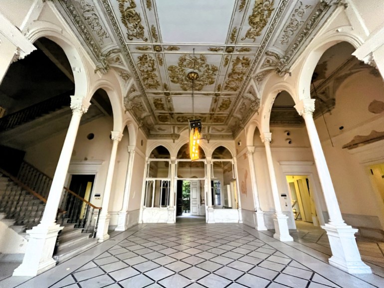 A wide view of the corridor with its gray-gilt ceiling and white arched galleries on either side