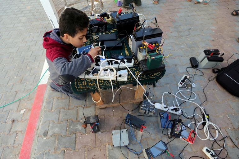 A Palestinian boy charges a mobile phone from batteries offered as a free service in his neighbourhood which experiences power shortages in Gaza January 31, 2018 [Reuters/Ibraheem Abu Mustafa/file photo]