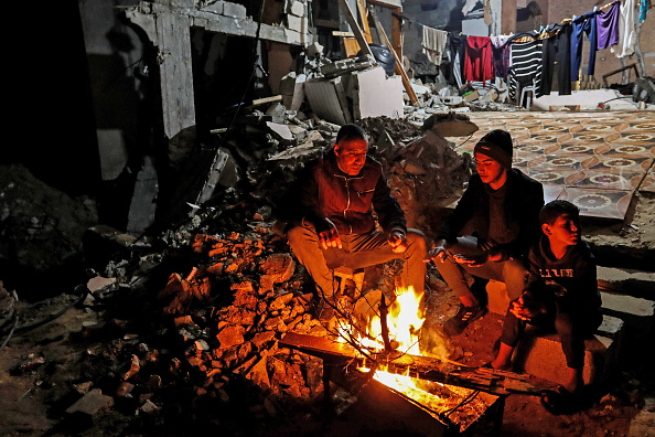 Palestinian citizens sit in front of their house that was destroyed by air strikes in the Khuza’a area and light a fire in the cold weather in Khan Yunis, Gaza.