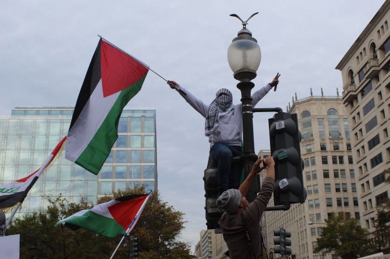 Masked protester carrying Palestinian flag scales light pole at Palestine solidarity protest in Washington, DC