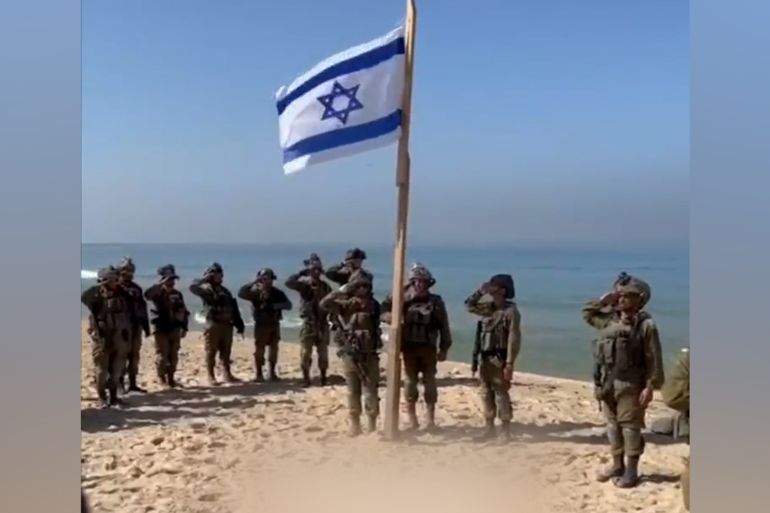 Captura de tela de um vídeo que mostra soldados israelenses hasteando a bandeira israelense em uma praia em Gaza em novembro de 2023 [Al Jazeera/Screenshot]