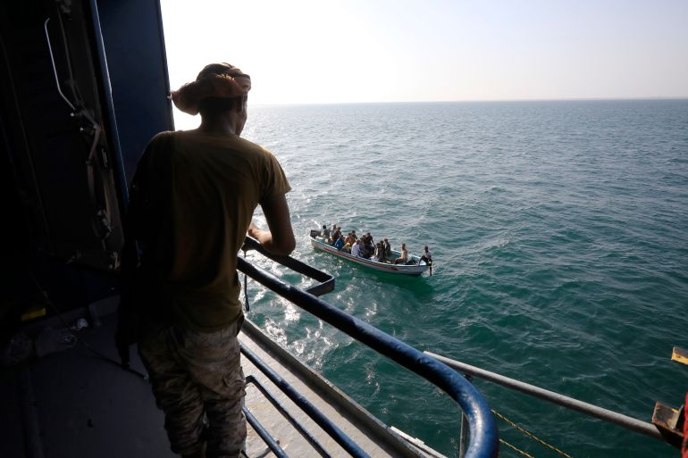 A boat carries people as a Houthi fighter keeps watch on the deck of the Galaxy Leader cargo ship