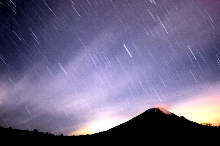 Yıldızların arasından geçen bir meteor, Meksika yanardağının üzerindeki gece gökyüzünü aydınlatıyor.  Mor gökyüzü beyaz çizgiler