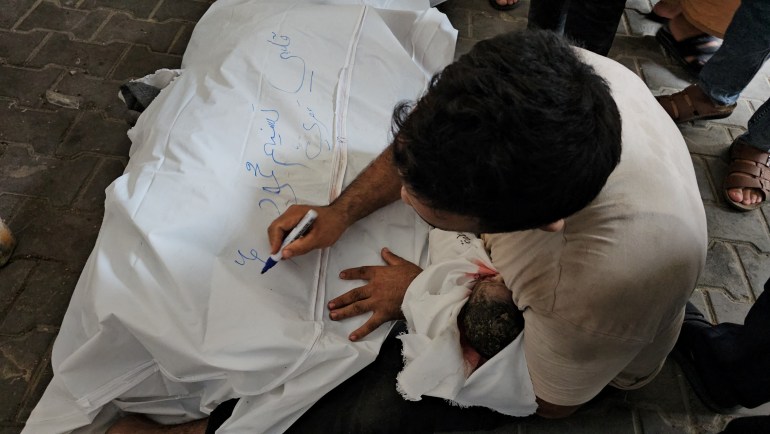 A Palestinian man writes on the white shroud covering his wife's body