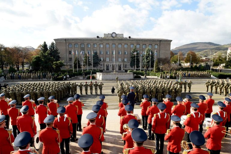 Soldiers from Azerbaijan on parade in Nagorno-Karabakh region's capital city. There is a miitary band in red ceremonial uniforms.