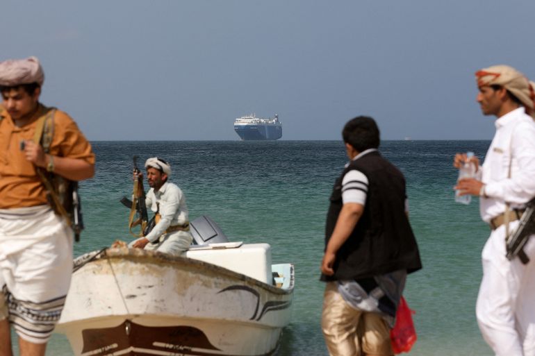 Silahlı adamlar Yemen sahilinde.  Arkalarında denizde büyük bir gemi görülüyor.