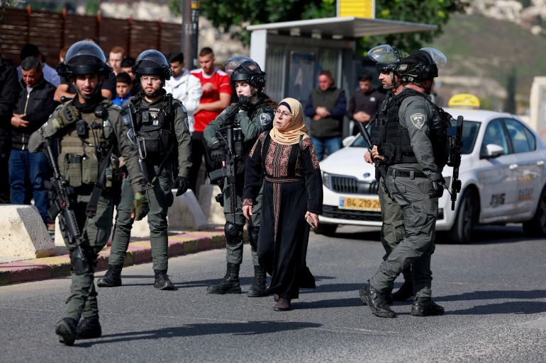 A woman walks next to Israeli Border Police officers while Muslim Palestinians hold Friday prayers