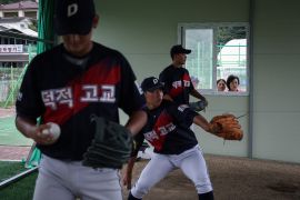Local people watch An Seung-han, 17, An Seung-young, 16, and Bang Jun-young, members of the Deokjeok High School baseball team, as they take part in a practice session, on Deokjeok island in Incheon, South Korea.