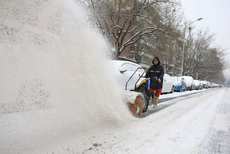 A worker operates a machine sweeping snow on a street