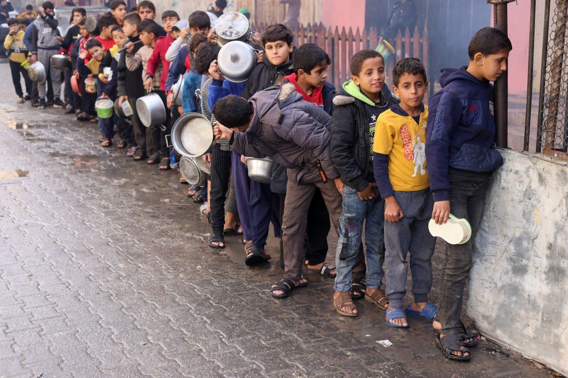 Palestinian children carry pots as they queue to receive food cooked by a charity kitchen, amid shortages in food supplies, as the conflict between Israel and Hamas continues, in Rafah.