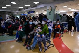 Crowds of parents and their children in an outpatients clinic at a Beijing hospital. They are wearing masks and seated. It looks very busy