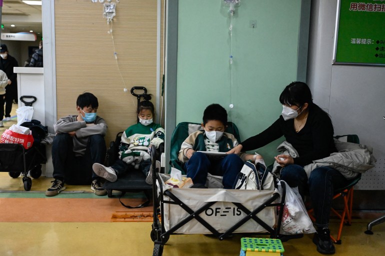 Children in a hospital corridor. They are attached to drips and wearing face masks.