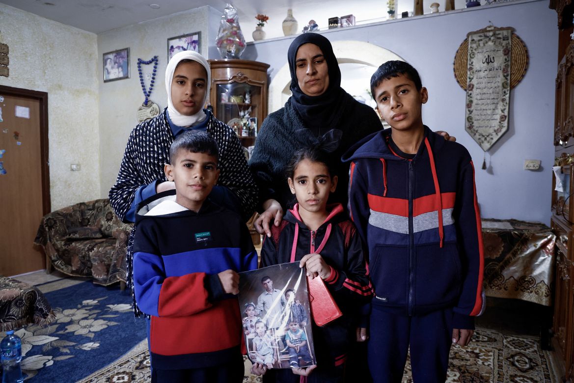 Ikhlas, the widow of Palestinian Bilal Saleh, poses with her children as they hold a picture of their late father at the village of As-Sawiyah, south of Nablus in the occupied West Bank, on November 29, 2023. - Saleh, was killed on October 28.