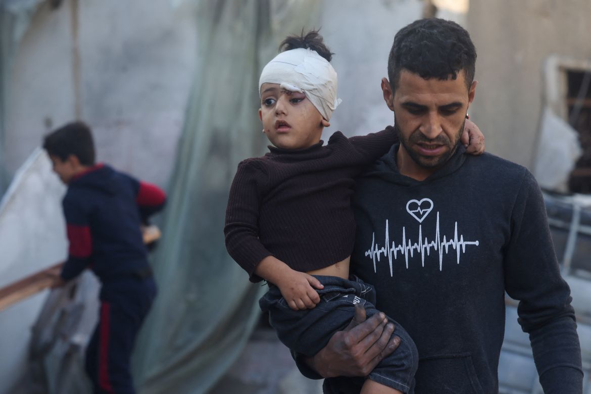 A Palestinian man carries a child injured during Israeli bombardment in Rafah, on the southern Gaza Strip, on December 2, 2023.