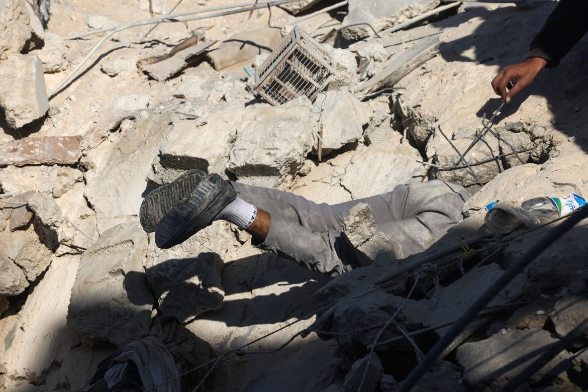 A Palestinian man searches for survivors beneath the rubble of a building following Israeli bombing in Rafah in the southern Gaza Strip on December 3