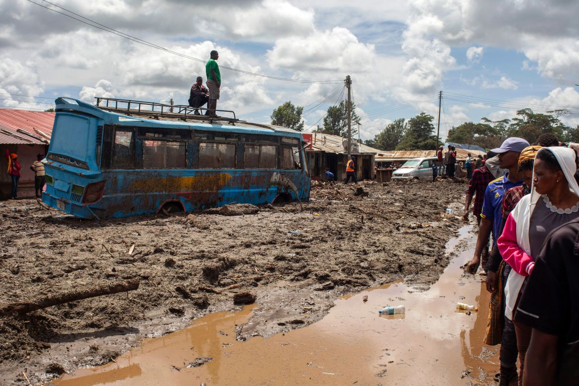Two men stand on top of a bus as others gather to assess damages at a street covered on mud following landslides and flooding triggered by heavy rainfall in Katesh, Tanzania.