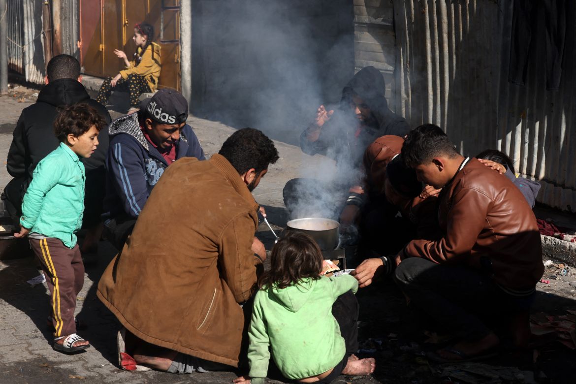 People who fled Khan Yunis in the southern Gaza Strip to Rafah further south, cook in the street near where they found temporary shelter, on December 9