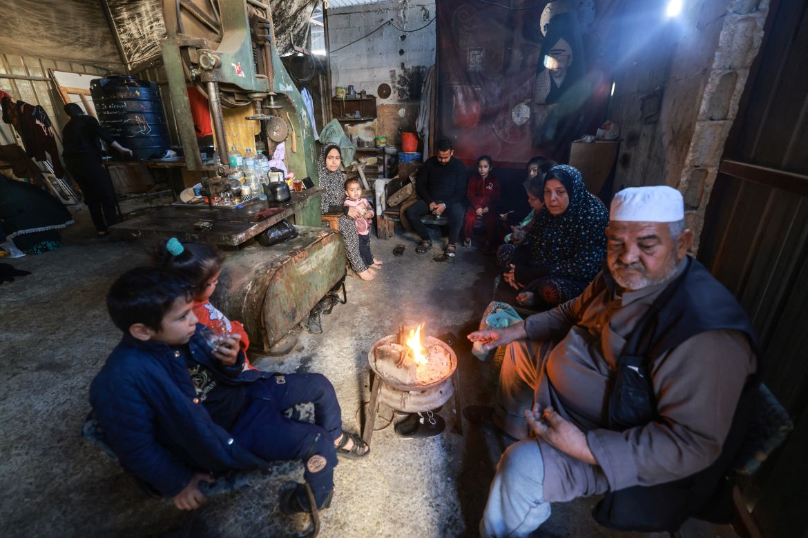 Members of a Palestinian family who fled Gaza City to Khan Yunis and had to recently flee to Rafah in the southern Gaza Strip, gather around a small fire, inside a workshop where they found temporary shelter, on December 9