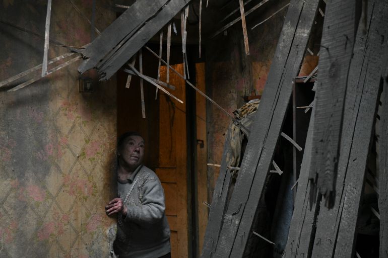 Uma mulher olhando de seu apartamento danificado no leste de Donetsk.  O papel de parede está coberto de fuligem e as vigas do teto desabaram.