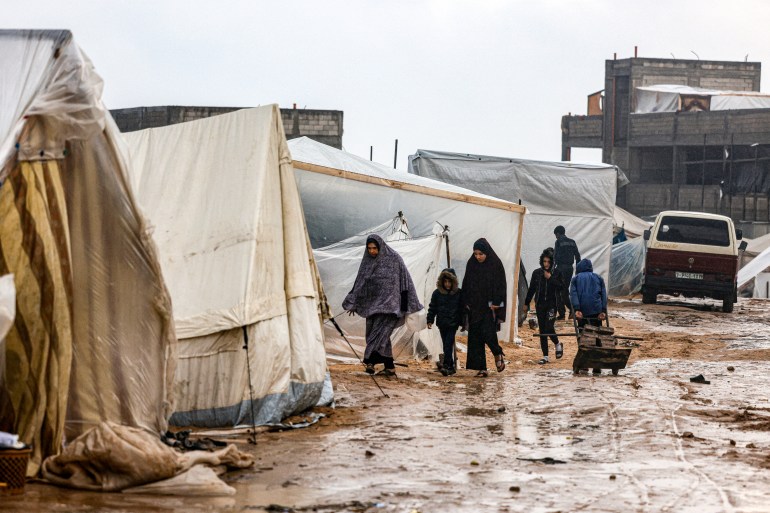 Palestinians walk under the rain at a camp for displaced people in Rafah
