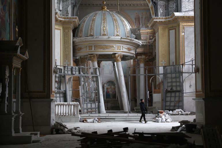 A worker repairing the interior of the damaged Cathedral of the Transfiguration in Odesa. A domed structure on pillars is leaning to one side.