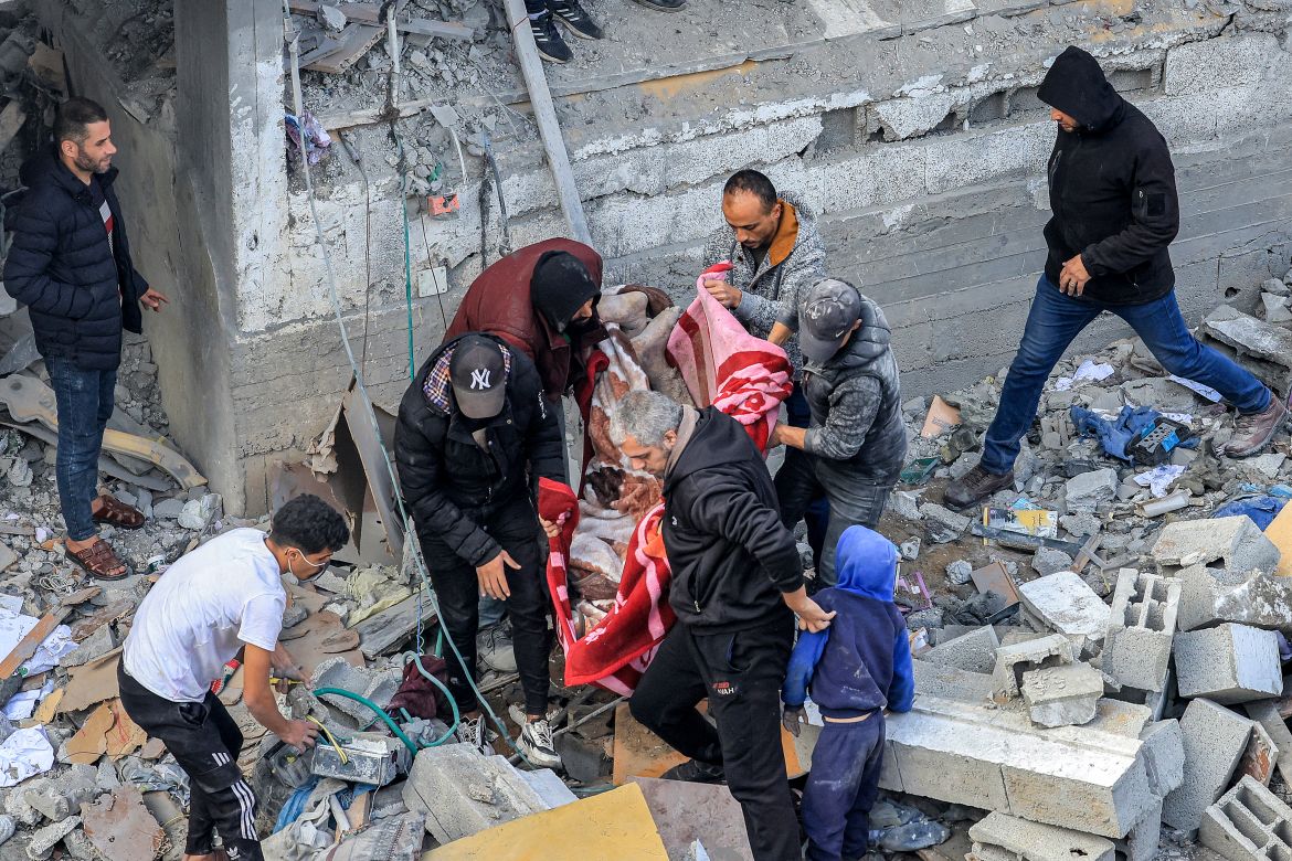 Men recover the body of a victim killed in the aftermath of an overnight Israeli strike at al-Maghazi refugee camp on December 25, 2023, amid ongoing battles between Israel and the Palestinian militant group Hamas