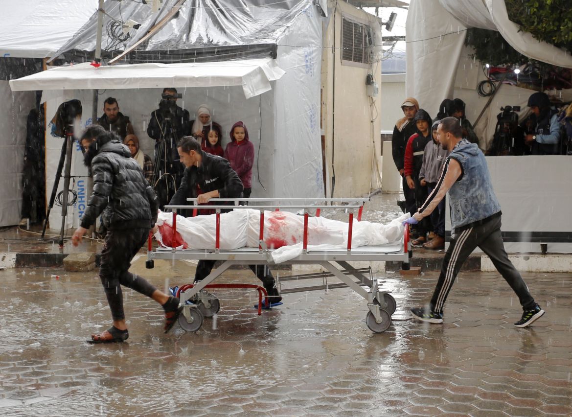 People carry body of Palestinian who killed in Israeli attack under heavy rain as Palestinians who took shelter in the Aqsa Martyrs Hospital and its surroundings in Deir Al-Balah city of the Gaza are struggling with the strong winds, heavy rain and floods affecting the region amid Israeli attacks.