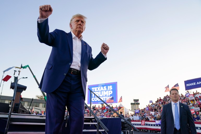 Trump lifts both his fists in the air at a campaign rally in Waco, Texas. Behind him, a screen reads, "Texas is Trump country," and crowds are visible.