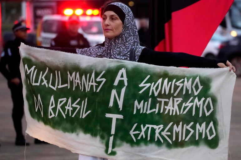 A woman holds up a green-and-white banner during a protest on the streets of Brasilia, which reads: "Musulmanas do Brasil, anti-zionismo, anti-militarismo, anti-extremismo".