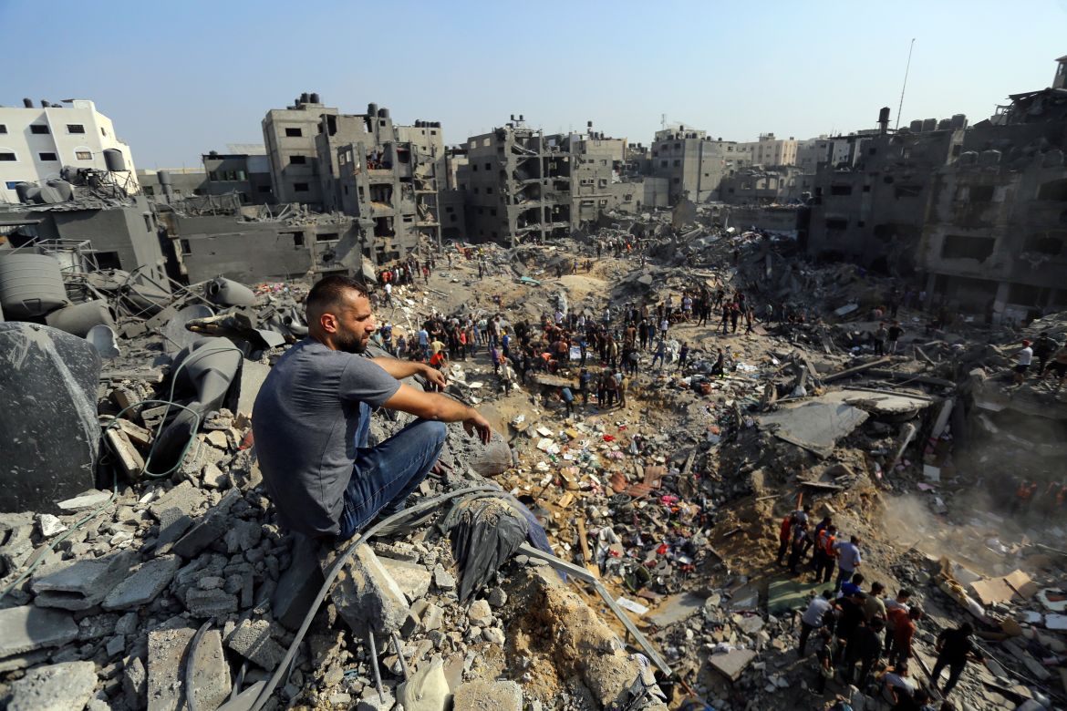 A man sits on the rubble as others wander among debris of buildings that were targeted by Israeli airstrikes in Jabaliya refugee camp, northern Gaza Strip
