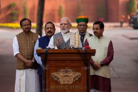 Indian Prime Minister Narendra Modi, center, speaking to media at a podium with 4 other BJP members, 2 on each side