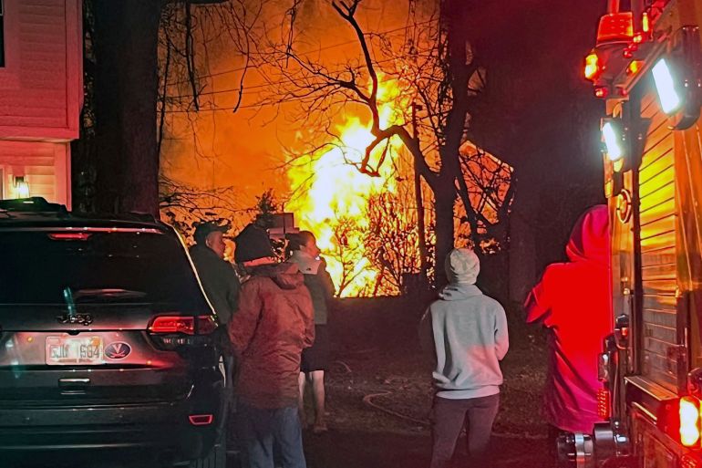 Flames at a distance while passerby's look at a virginia house that exploded