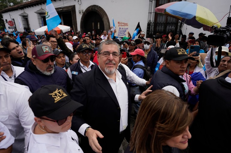 Bernardo Arevalo, in a white collared shirt and dark blazer, walks amid a crowd of supporters in Guatemala City's streets.