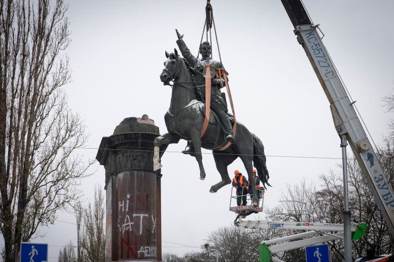 A statue of a Soviet-era commander on a horse being removed from its plinth in Kyiv. it is dangling from a crane.