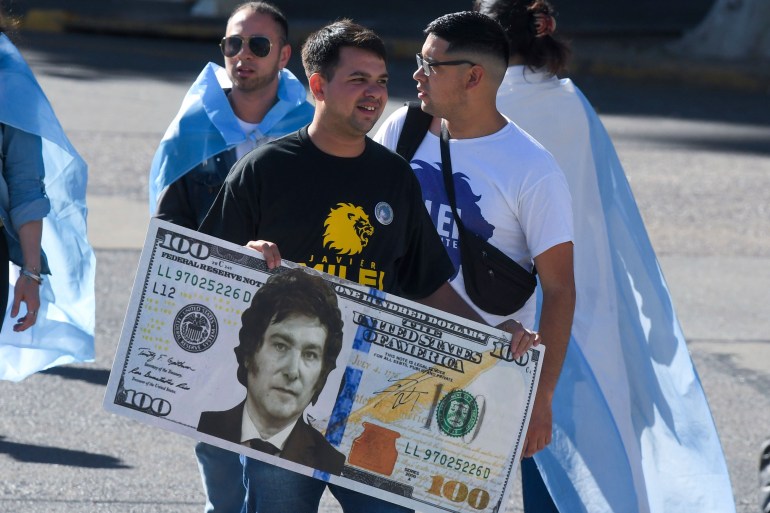 A supporter of Javier Milei carries a larger-than-life facsimile of a 100-dollar bill, with Milei's face in the centre.