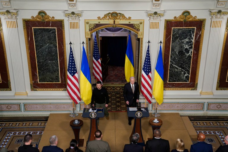 Volodymyr Zelenskyy and Joe Biden stand behind wooden podiums and in front of Ukrainian and US flags in a press conference at the White House.