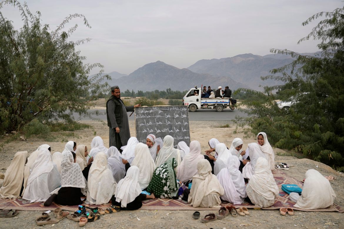 Afghan refugees pass by an outdoor girls classroom in Torkham, Afghanistan, Saturday, Nov. 18