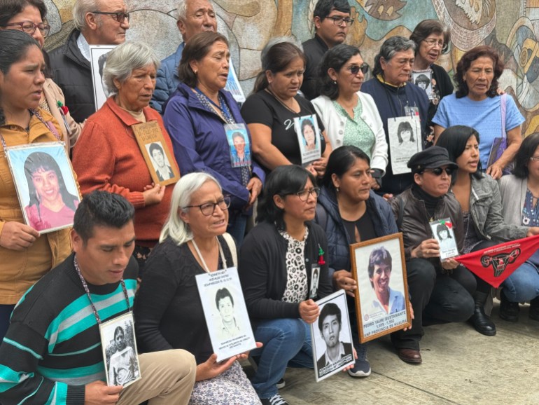 Family members line up in three rows — some sitting, some standing — but each one holds up a large black-and-white photo of a loved one who disappeared or was murdered under the Fujimori administration.