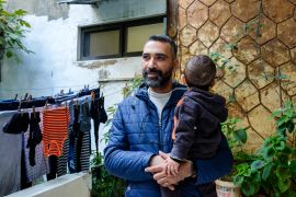 Mohammad Aby Swareh at the entrance of his mother Fatmeh&#039;s home, with his youngest son Jamal, in Beddawi refugee camp, northern Lebanon, November 29, 2023 [Rita Kabalan/Al Jazeera]