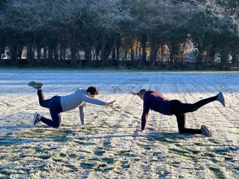 Waheed and Andy doing stretches on a frost-covered football field-