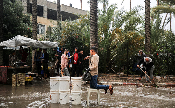 Palestinians are walking along a flooded street following heavy rains in Deir El-Balah, in the central Gaza Strip.