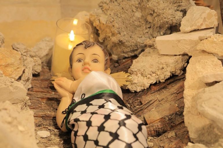 Closeup of Baby Jesus doll wrapped in Palestinian keffiyeh in the rubble manger