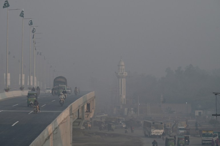 Passageiros caminham por uma rua em meio à poluição atmosférica em Lahore, em 17 de novembro de 2023. [Arif ALI / AFP]