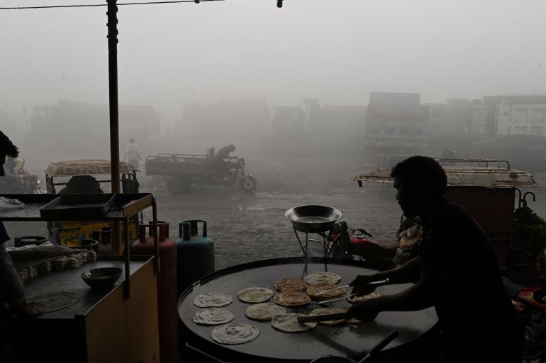 Bir işçi, 14 Aralık 2023'te Lahor'da yoğun dumanın ortasında bir yol boyunca ekmek yapıyor. [Arif ALI / AFP]